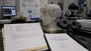 A lab scene with a brain model, neurostimulation equipment, research papers, and brain scan images on a monitor.