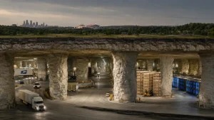 A vast underground warehouse carved into limestone, with trucks, storage racks, and glowing blue server bays beneath the Kansas City skyline.