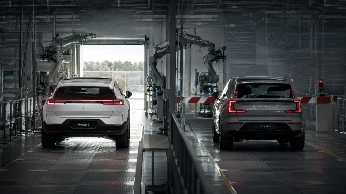 Rear view of a Polestar 3 and a Volvo SUV inside an automotive production line with robotic arms.