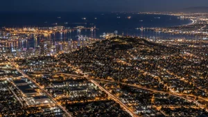 Night aerial view of Long Beach and Signal Hill with city lights, highways, and the harbor visible in the distance.