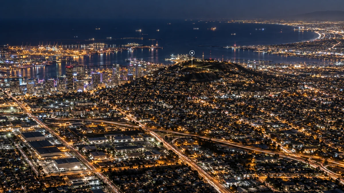 Night aerial view of Long Beach and Signal Hill with city lights, highways, and the harbor visible in the distance.